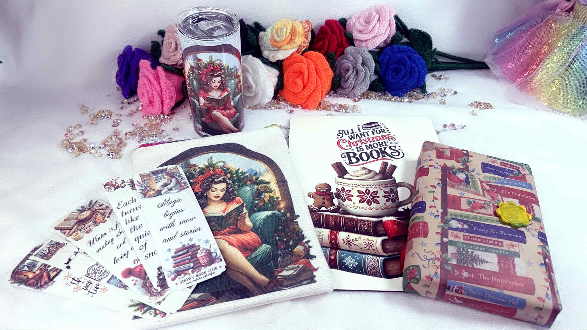 A festive Christmas book lover’s gift box displayed with a handmade booksleeve, Christmas-themed tumbler, laminated bookmarks, A4 coaster and a wrapped surprise book, surrounded by colourful knitted roses and soft winter décor.