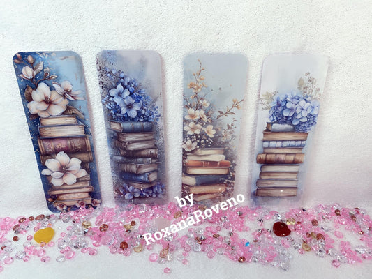 A set of four laminated paper bookmarks with a blue flower and book design, displayed upright on a surface with decorative elements around.