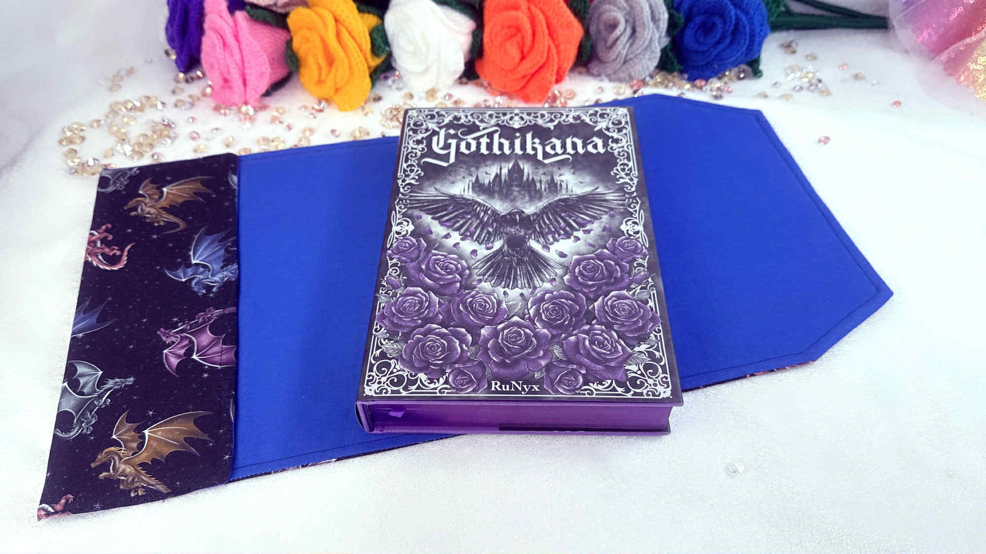 Purple book titled 'Gothikana' with decorative cover on a white surface surrounded by colorful flowers.