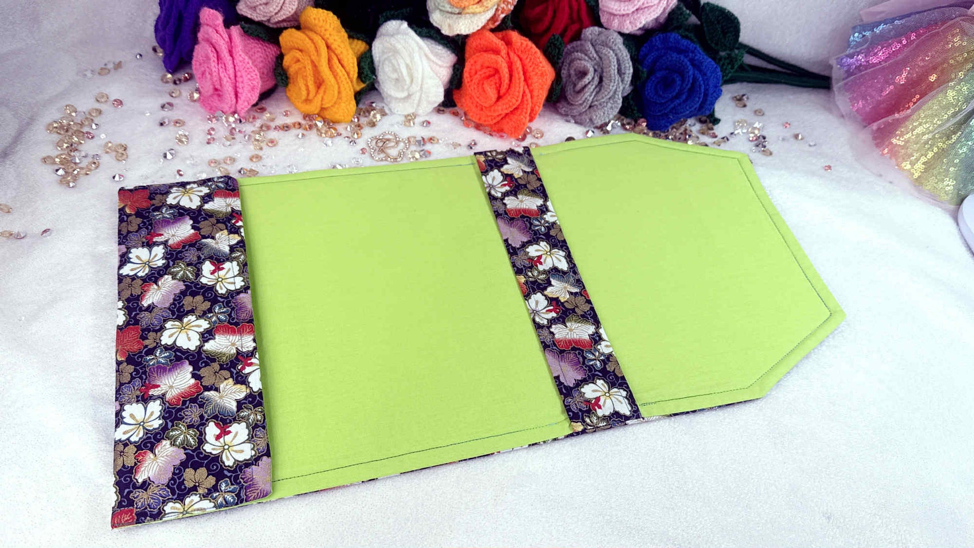 Green fabric with floral trim on a white surface with colorful flowers and ribbons. Handmade book cover by Roxana Roveno